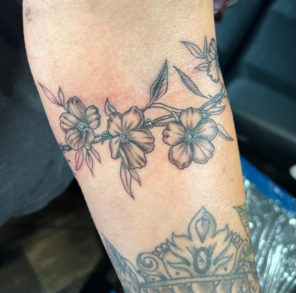 Fine-line dogwood floral vine tattoo wrapping an outer forearm