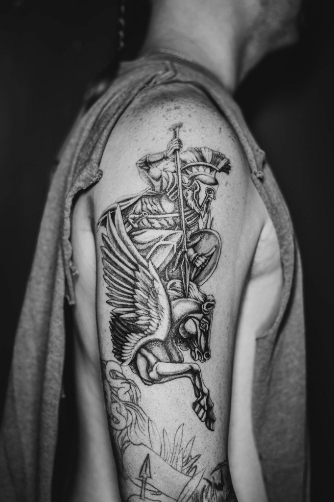 Illustrative blackwork tattoo of a Spartan warrior riding Pegasus on an upper arm
