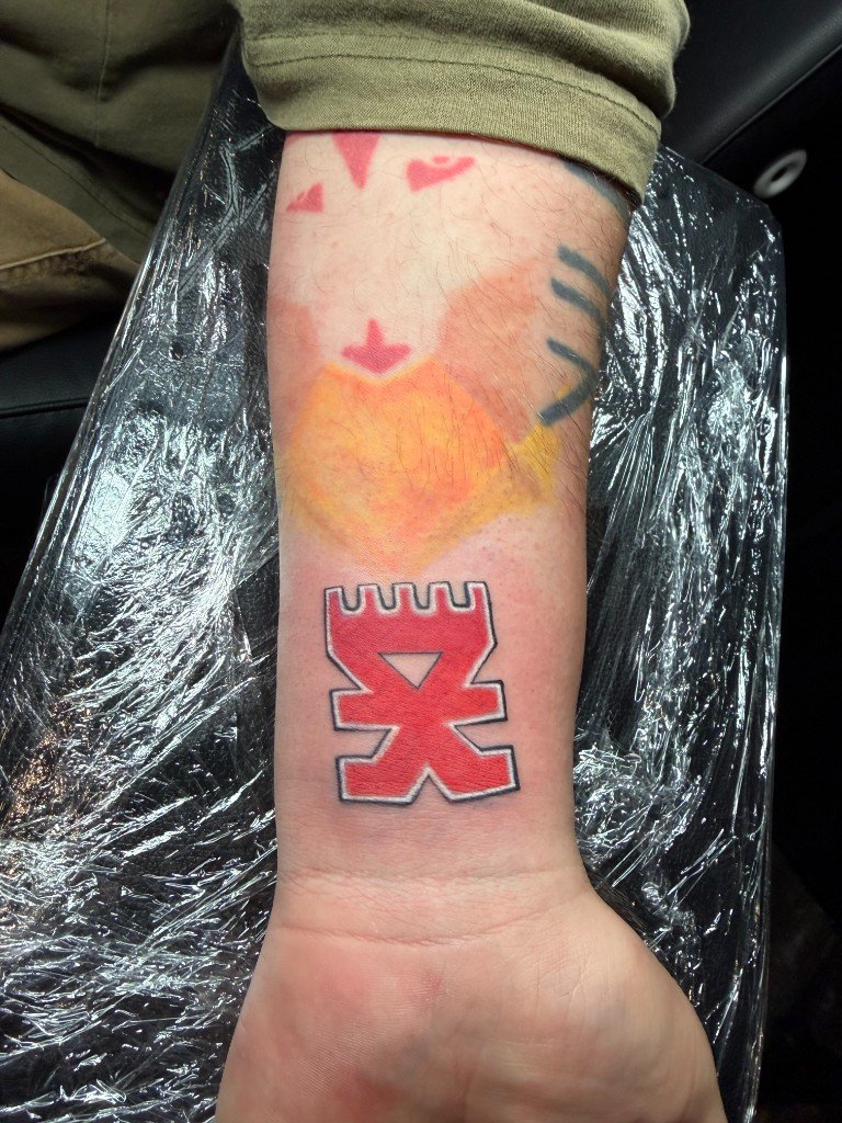 Bright red Khorne rune tattoo with an orange flame above it, on the inside of a wrist